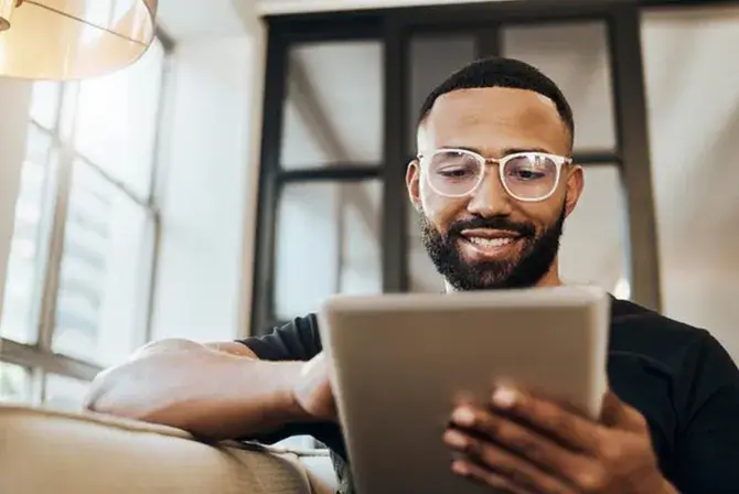 Man sits on a couch and looks down at a tablet device