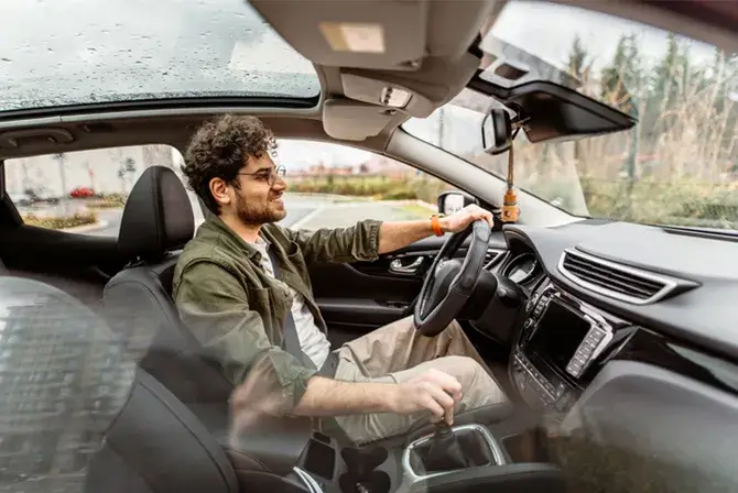 A young man is test-driving a car. He has one hand on the wheel, and the car’s interior features are prominently displayed.