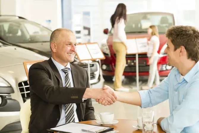 Two men shaking hands inside a car dealership.