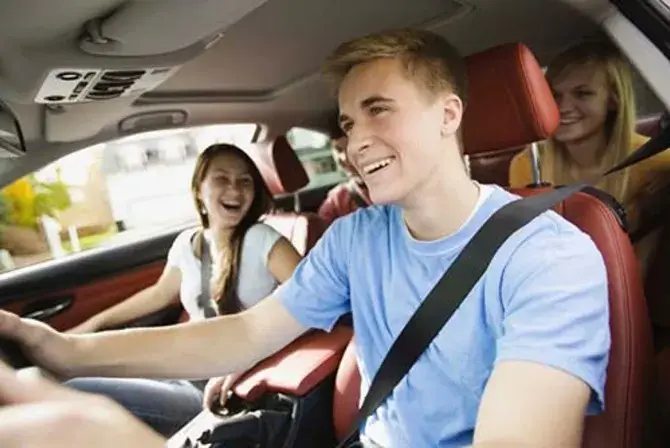 A young man driving a car with his friends inside.