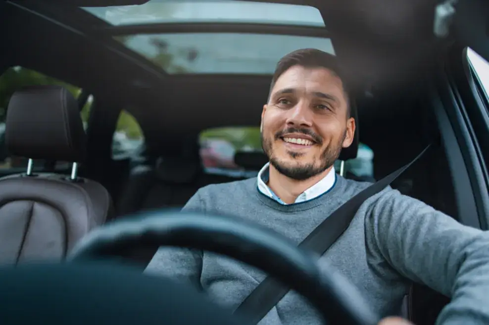 Man sitting in the driver’s seat of a car, smiling as he drives.