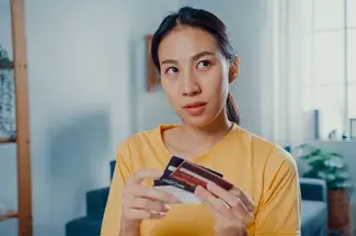 A person in a yellow shirt holding a few credit cards, appearing thoughtful, in a room with soft lighting and modern decor.