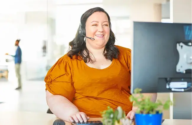 VACU employee with a headset on smiles while working on a computer