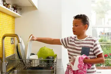 Young boy putting away clean dishes