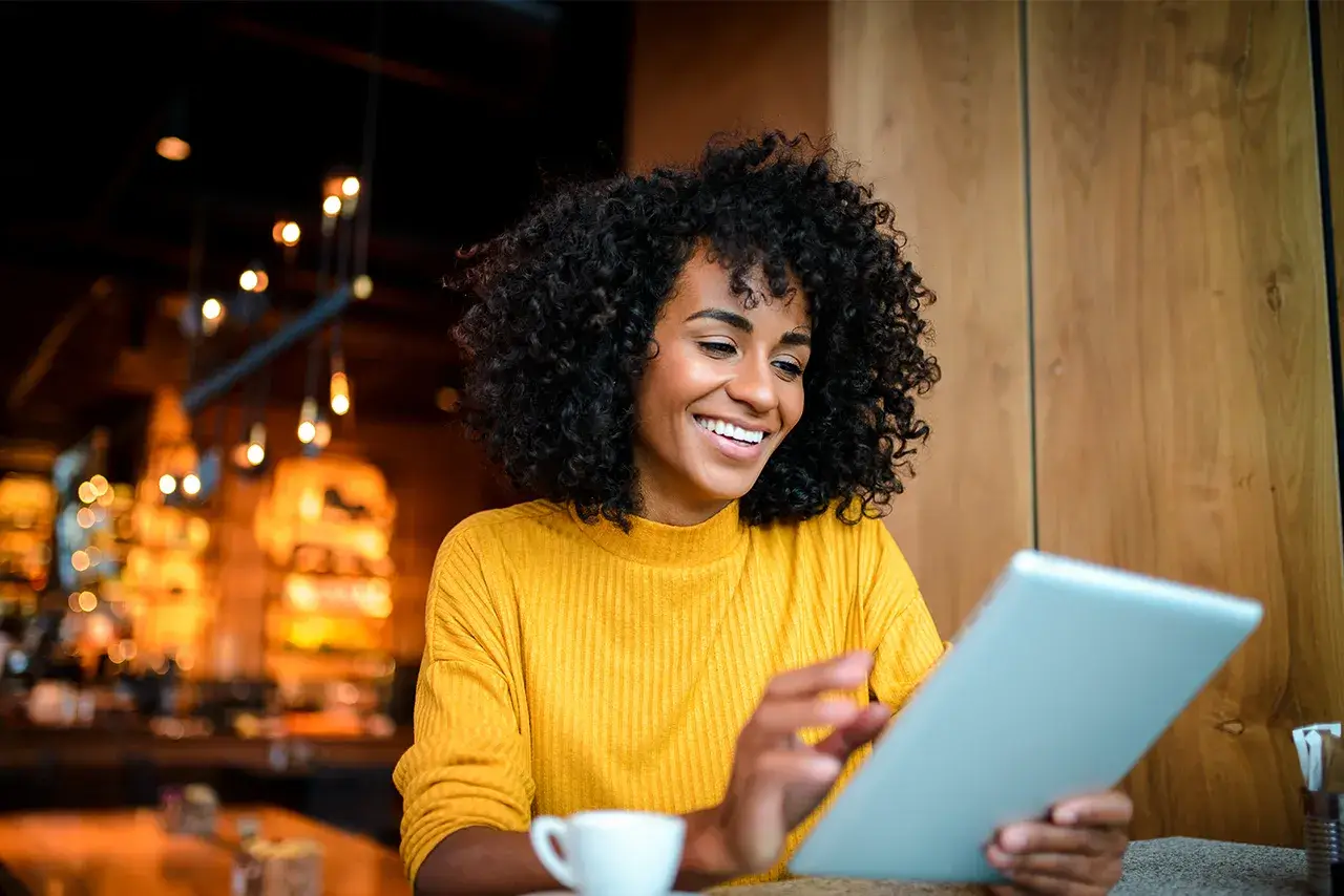 Women sits at a cafe with a cup of coffee while working off of a tablet