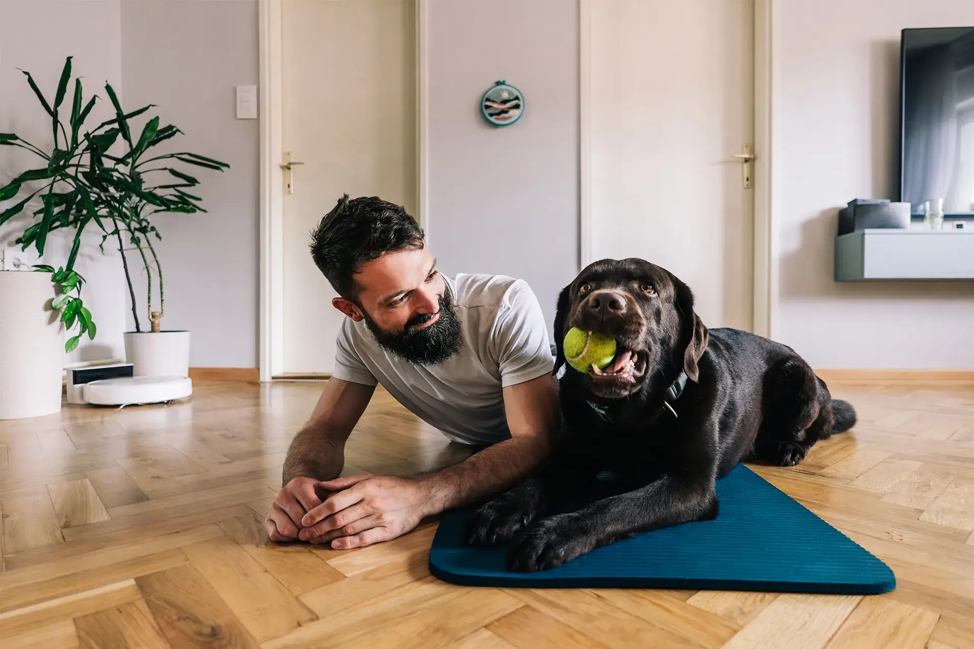 Man smiles and looks at dog laying down on the floor next to him on a yoga mat