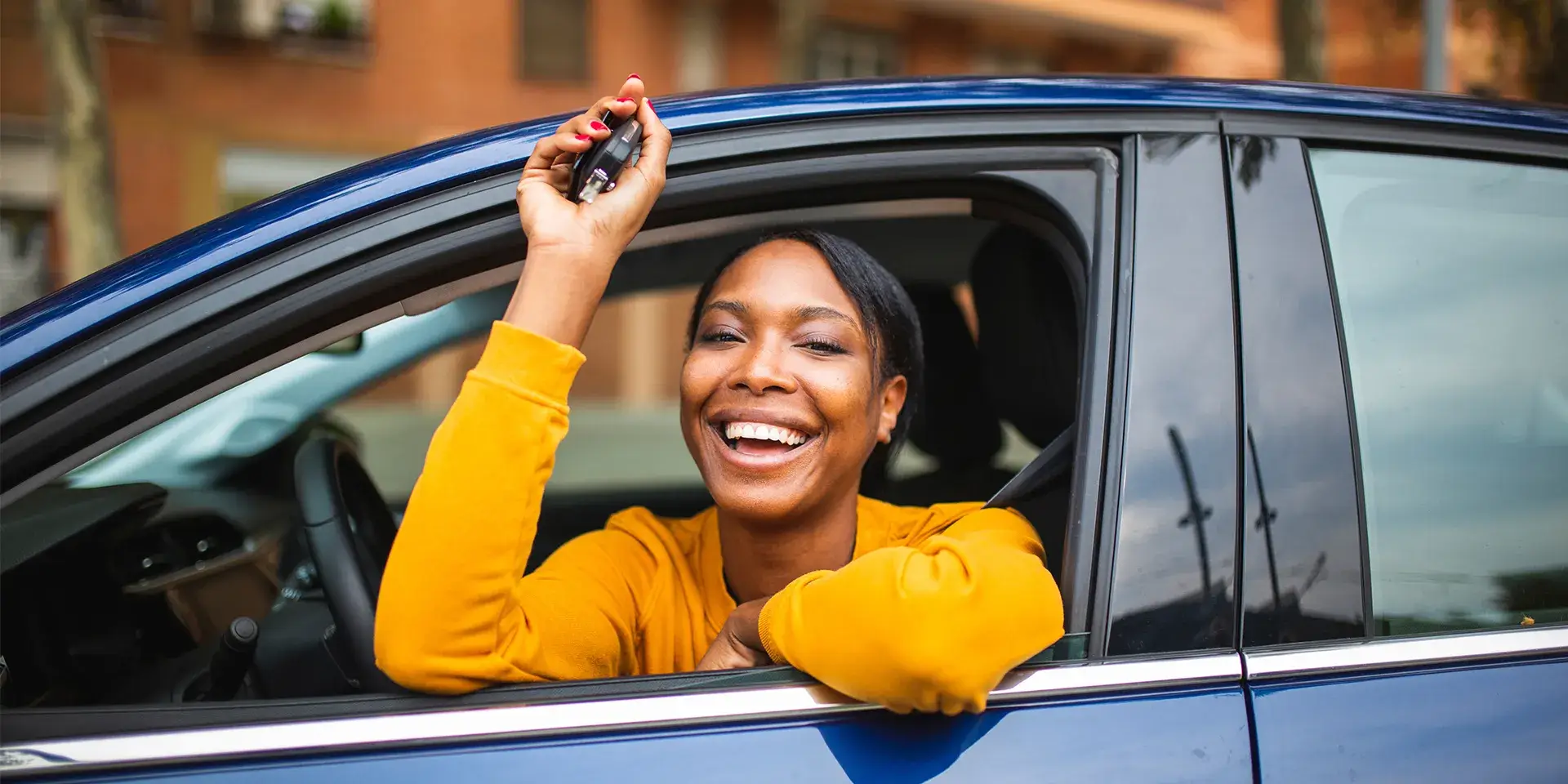 Woman smiling with keys in her hand as she looks out of car window