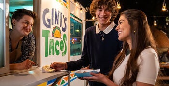 Man and women standing at food truck, using credit card to order food.